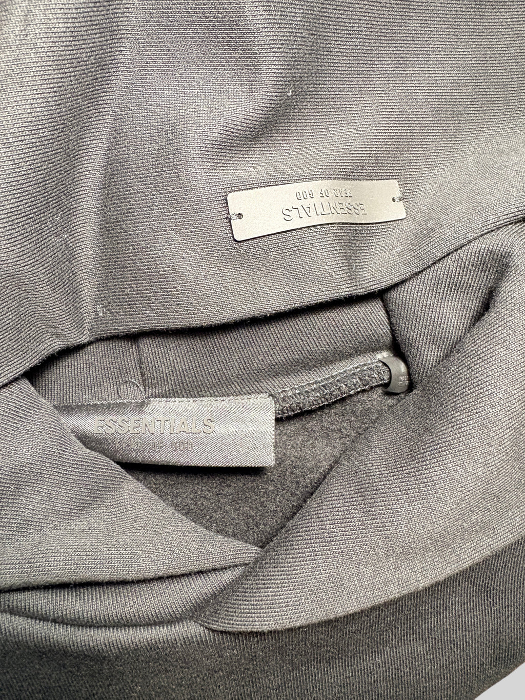 Gros plan sur l'étiquette intérieure et le logo métallique FASHION SC Essentials d'un sweat à capuche en coton gris