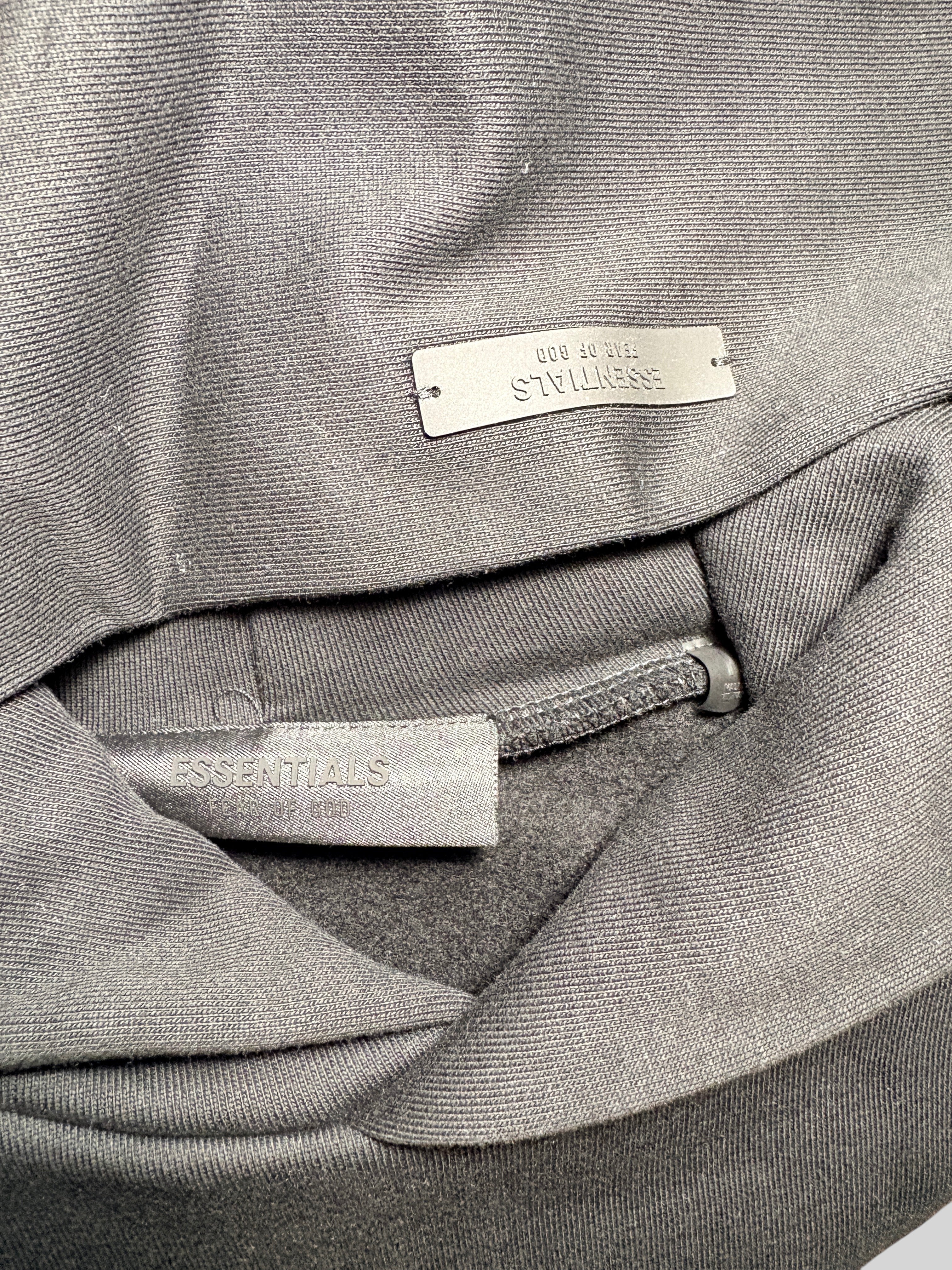 Gros plan sur l'étiquette intérieure et le logo métallique FASHION SC Essentials d'un sweat à capuche en coton gris
