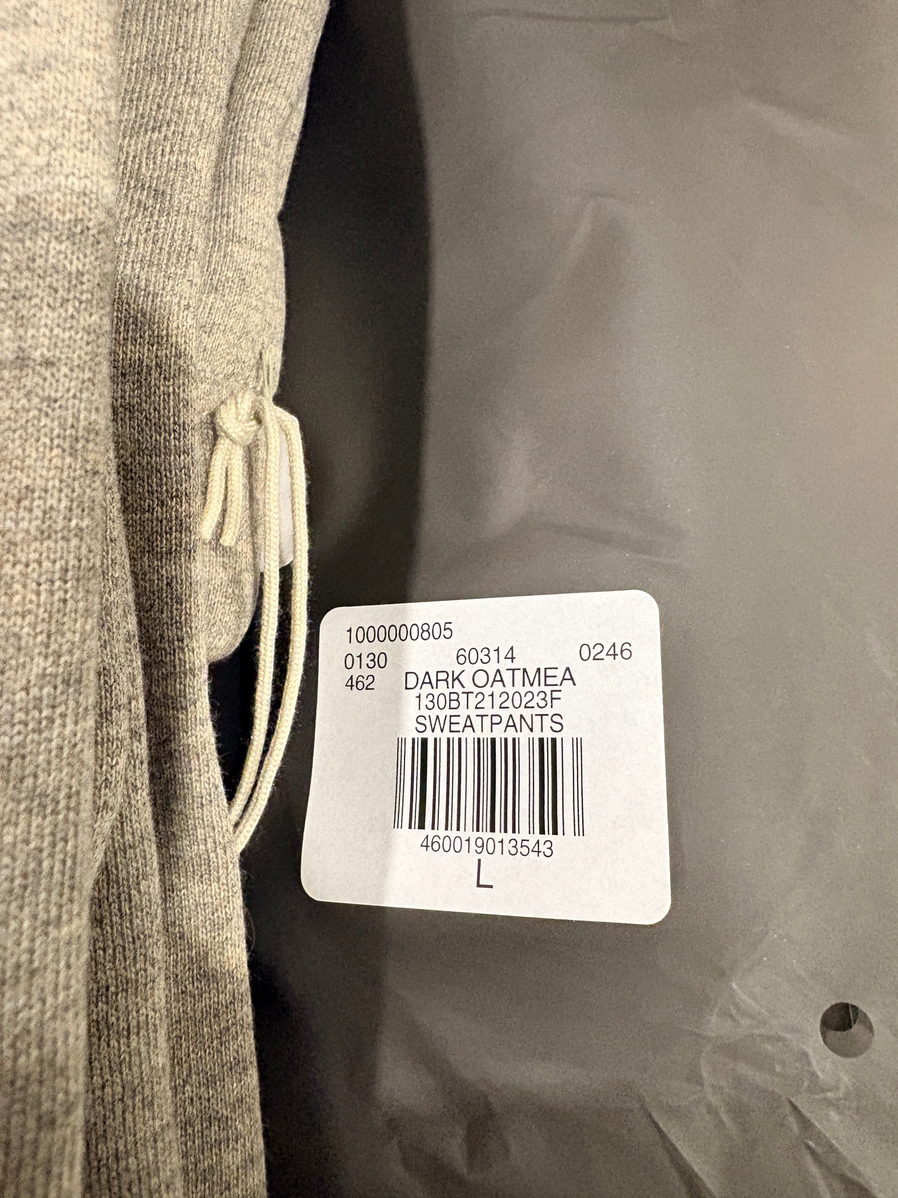 Etiquette de prix sur un pantalon de jogging Fear of God ESSENTIALS 1977 en molleton gris beige Dark Oatmeal