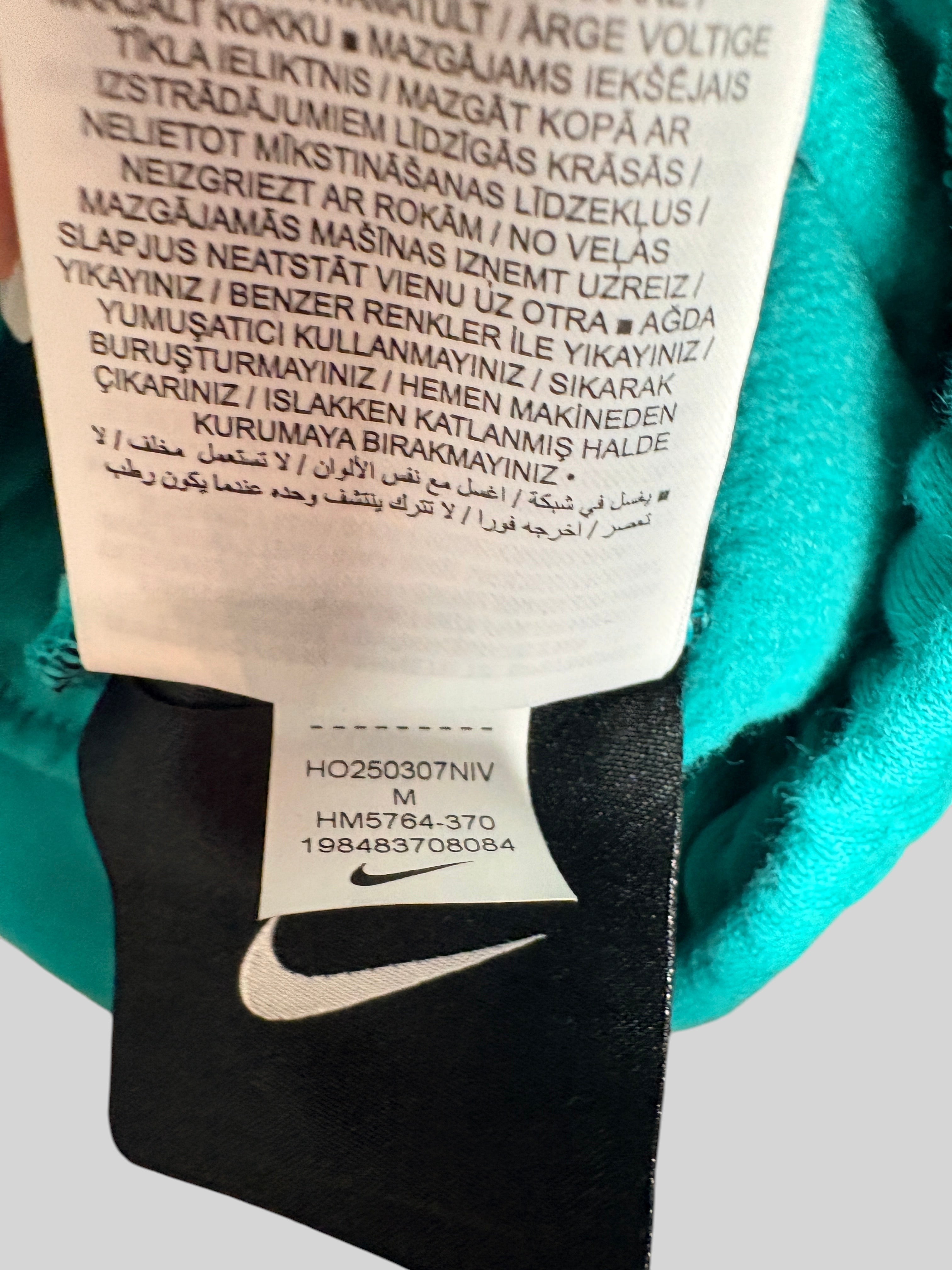 Étiquette intérieure du pantalon FASHION SC Nike x NOCTA Fleece CS vert Neptune avec logo Swoosh et détails du modèle