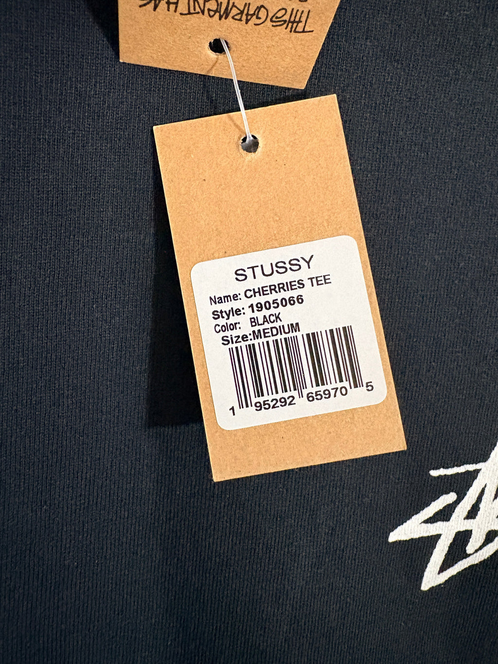 Étiquette en carton FASHION SC sur un t-shirt noir Stüssy Cherries Tee avec détails du modèle et code-barres