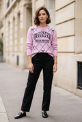 Pull rose porté avec un pantalon droit noir et des mocassins, dans un décor extérieur chic